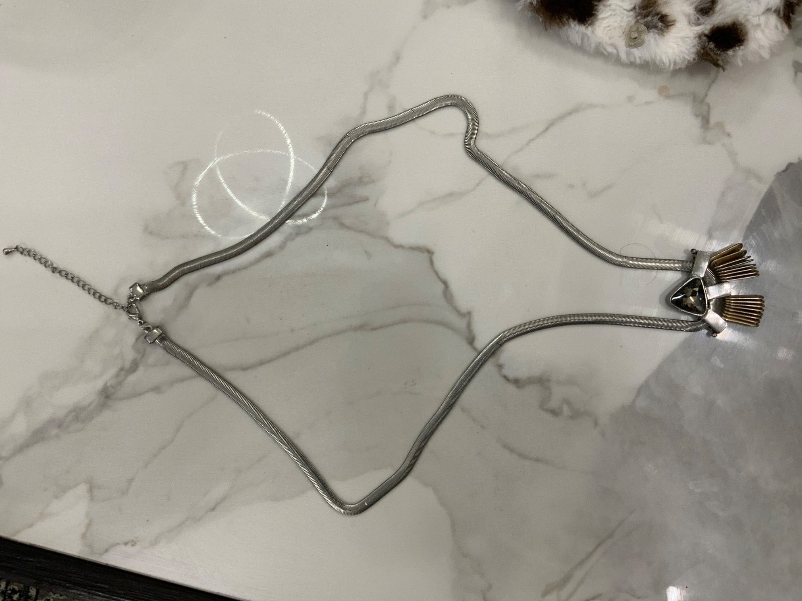 This piece features a flat silver snake chain and a prominent geometric pendant.